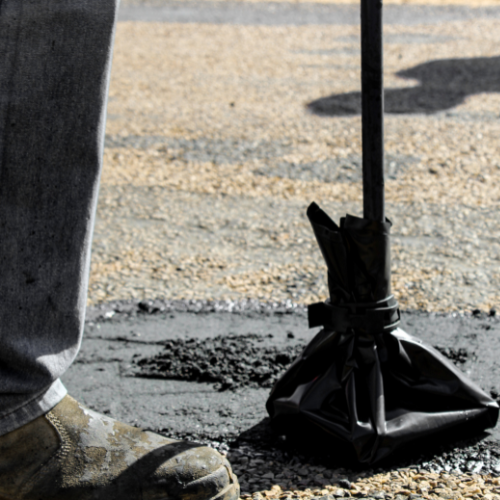 Person using a tamper tool on asphalt during roadwork.