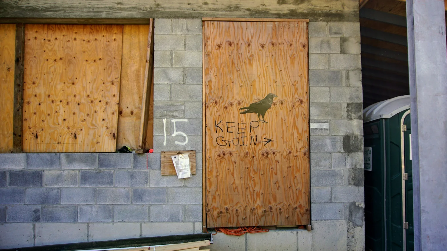 Boarded-up construction entrance with plywood panels and concrete block walls.