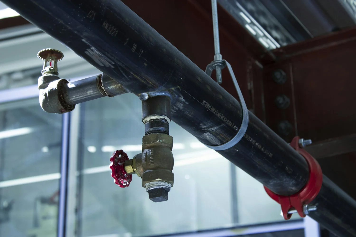Close-up of industrial black metal pipe with red valve in a building.