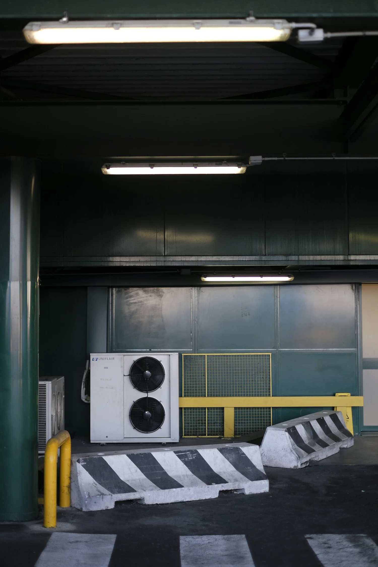 Industrial area with commercial air conditioning unit and yellow barriers.