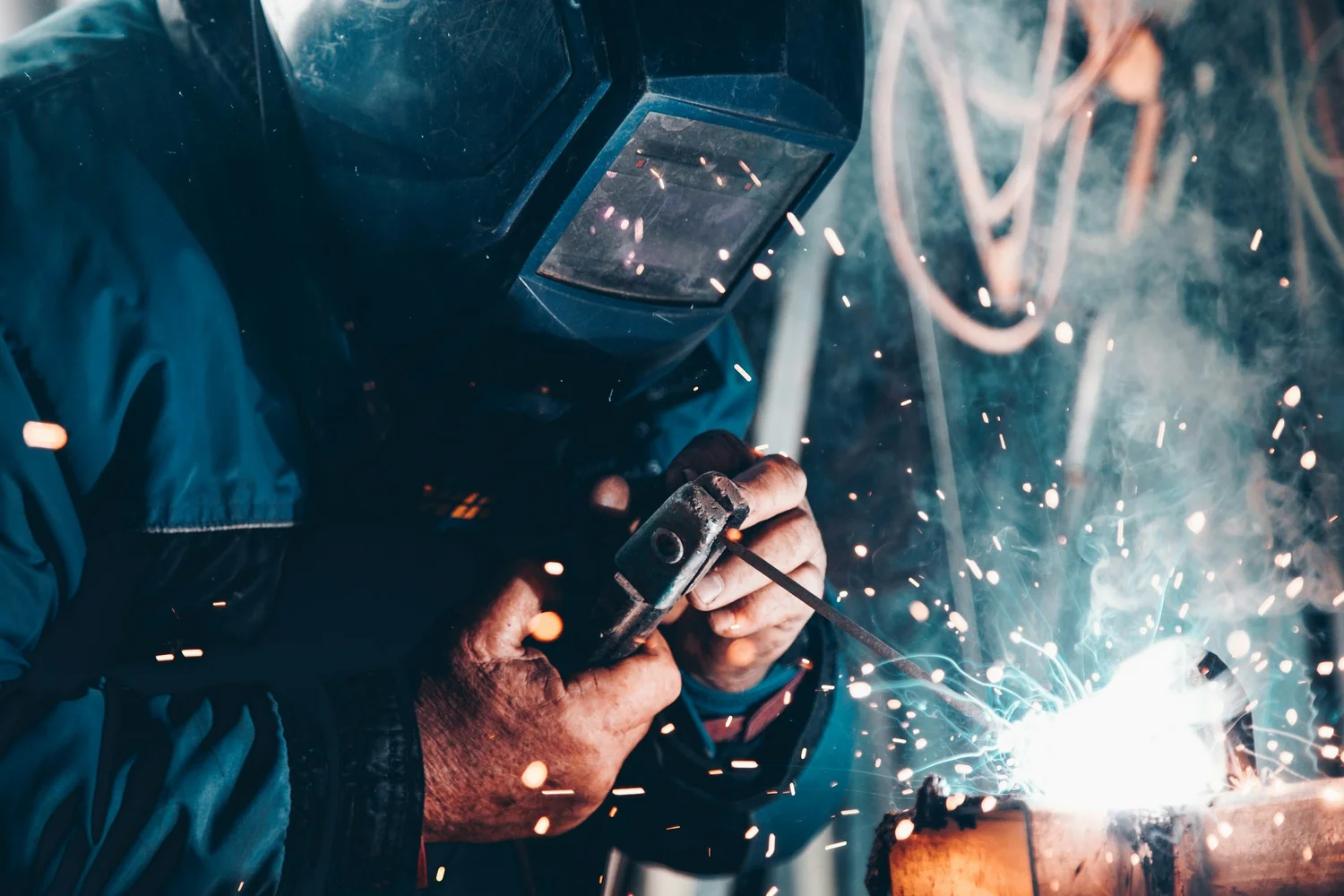 Person welding metal with protective gear, sparks flying.