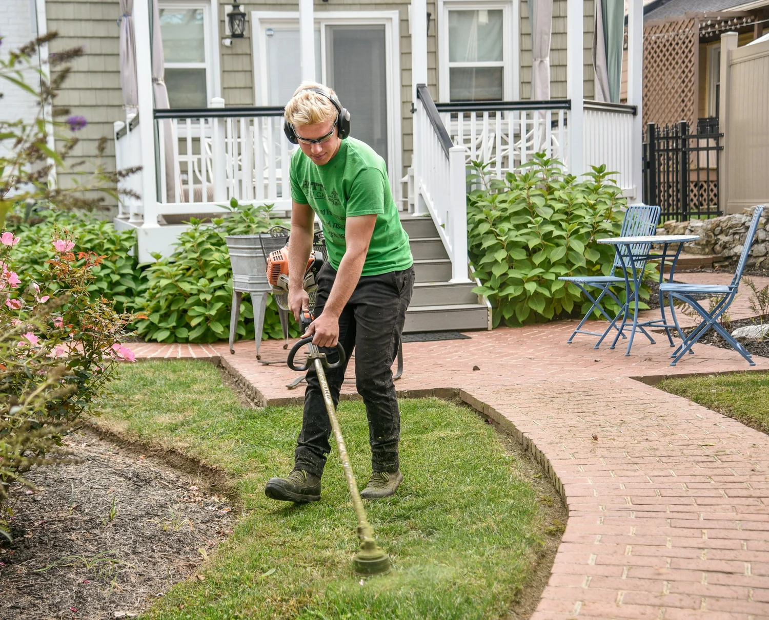 Worker using a string trimmer to edge grass along a garden pathway.